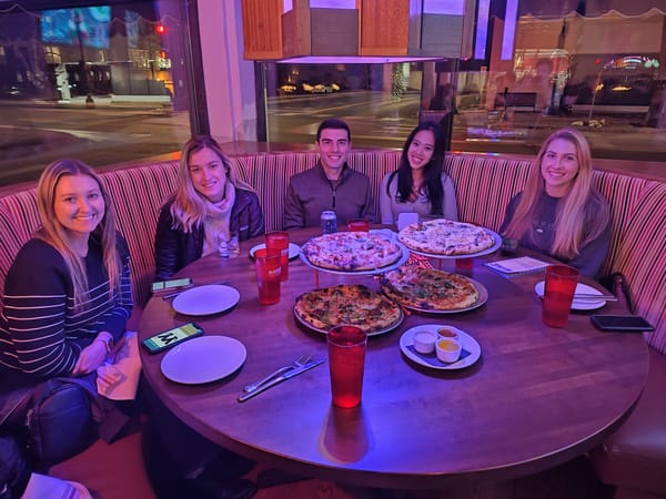 five people at a restaurant sitting around a table with four pizzas